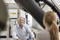 Ein Mitarbeiter von Sto Industrie und ein Kunde blicken auf eine automatisierte Beschichtungsanlage im Holzfertigbau