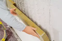 Eine Dämmplatte aus Mineralwolle wird auf eine mit Klebemörtel beschichte Wandfläche geklebt