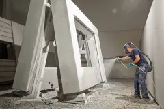 Ein Mitarbeiter eines Fertigbauherstellers beschichtet eine Betonfertigteilwand mit einem mobilen Sprühgerät